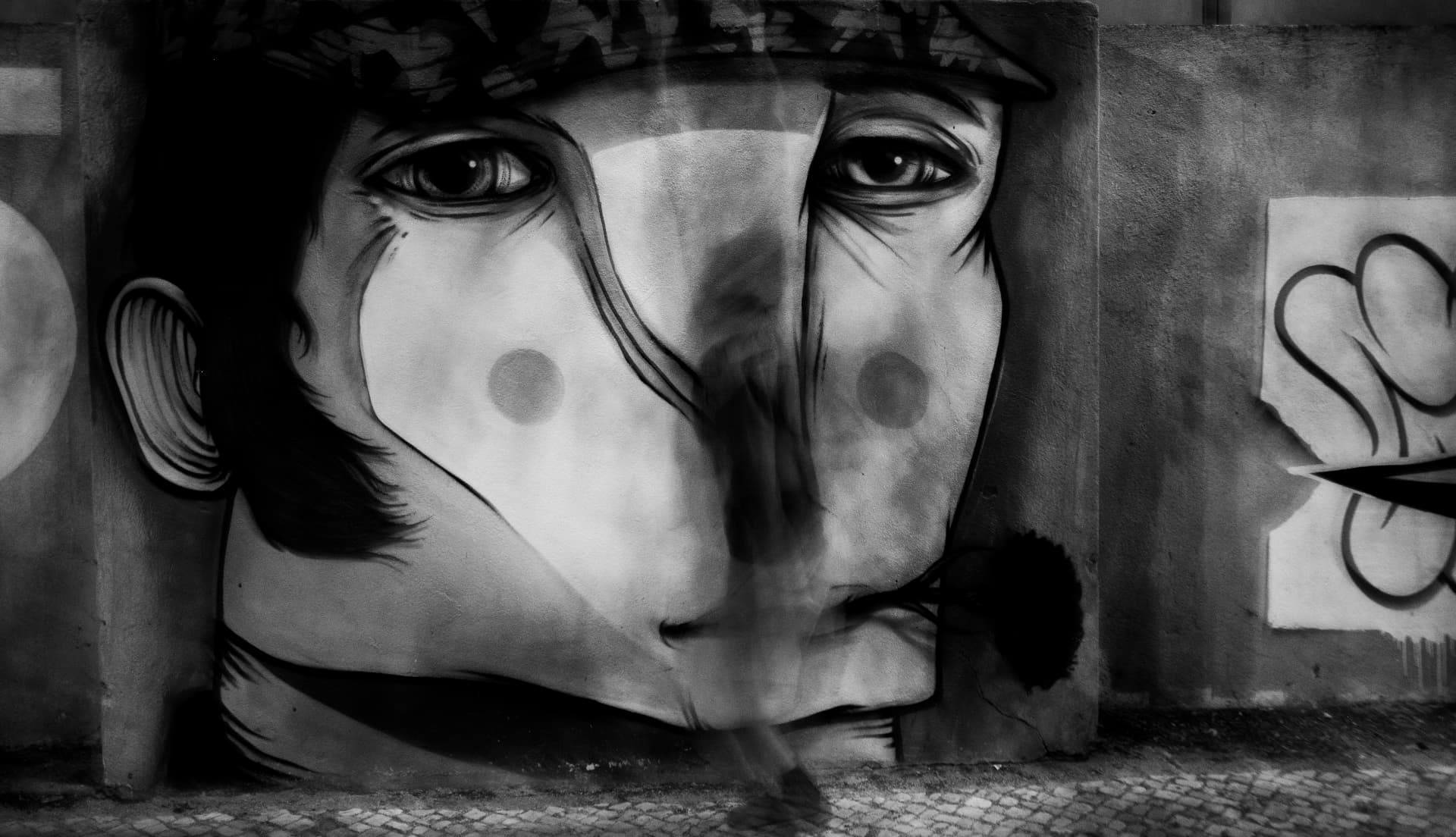large monochrome mural face with a blurred passerby in Lisbon